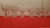 Front angled view showing full set of various crystal glasses with different cut patterns arranged in a row on red fabric.