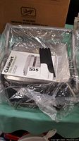 Photo of Cuisinart grill wrapped partially in plastic with cleaning utensil and manual on top.
