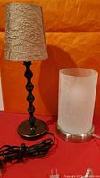 Two table lamps side by side on a red surface against an orange background, showing cords and bases clearly.