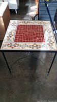 Front view of the mosaic stone tile top and black metal legs of the side table.