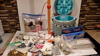 Overview of assorted sewing notions arranged on the counter including buttons, thread, portable hand sewing machines, and curtain accessories placed in front of the Dritz basket.
