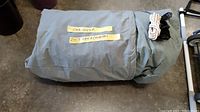 Car cover rolled and stored in gray bag with attached strap and labels.