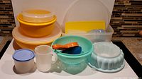 Front view of the lot showing all pieces: three yellow nested bowls with lids, teal mixing bowl, white mold, clear pitcher, measuring cups, small container with blue lid, and extra lids.