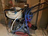 Side view of air compressor on wheeled cart showing coiled blue and white hoses and compressor body.