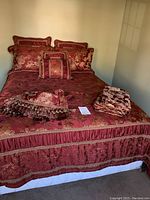 Full bed with bedding and decorative pillows arranged on top. Rich red and gold floral fabric visible over entire bed.