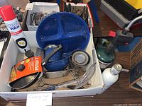 Photo showing the camping cook set items in a box including a blue sectioned plate, metal ladle, spatula, foil pan, small metal cup, and clear plastic bowl.