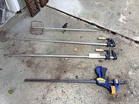 Image showing three clamps and a metal mixer blade laid out on concrete.