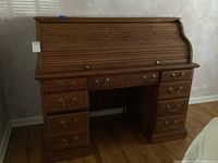 Front view of oak roll top desk showing closed roll top, eight drawers (four on each side) and central knee space.