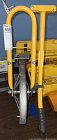Full view of the yellow metal measuring wheel with stand, showing the large rubber wheel and handle.