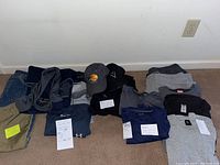 Lot of men's casual and activewear clothing laid on floor, including pants, shirts, hoodie, and caps