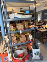 Front view of the gray metal shelf showing five tiers filled with various boxes and tools. Label tags visible on the shelf structure.