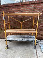 Front view of the yellow metal scaffold with three wooden platforms and caster wheels