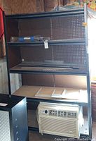 Full view of the metal shelf unit showing three shelves installed, a pegboard back panel, and paper towel holder mounted underneath the top shelf.