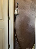 Full view of curved shower rod leaning against wall near door frame, showing hardware in plastic bag attached to top.