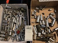 Two boxes with assorted sockets, wrenches, screwdriver, and adapters in garage setting