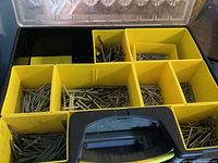 Open yellow plastic storage box showing compartments filled with various sizes of nails and screws.