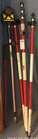 Photo showing multiple red and white SECO branded adjustable survey poles along with a black pole with prism target and yellow prism.