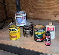 Photo showing all six cans and bottles of wood finish and protective oils arranged on wood surface