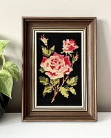 Front view of the framed embroidered flower wall portrait, showing large pink roses with leaves on black fabric background in a wooden frame.
