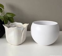 Photo showing the front view of two plant pots: one matte white with rounded shape, one iridescent shaped like a tulip flower