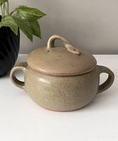 Front view of light brown pottery bean pot with lid featuring a snake-shaped handle and two side handles.