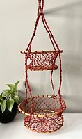 Front view of two-tier red braided hanging plant holder with bamboo rings, hanging against wall.