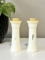 Front view showing pair of white plastic salt and pepper shakers with silver 'S' and 'P' on front, yellowed lids visible.