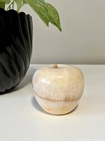 Front and side views of a polished marble apple display piece with beige and brown veining and a small wooden stem.