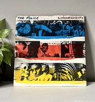 Front cover of The Police Synchroncity vinyl record showing colored strips with band images.