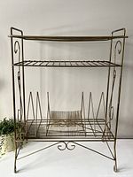 Full front view of the vintage brass-toned metal stand empty, showing the structure and multiple shelf levels, including angled dividers at the base for records.