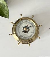 Front view showing the barometer dial with 'Rain', 'Change', 'Fair' markings and brass ship wheel design frame.