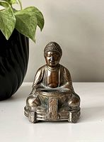 Front view of the brass Buddha statue showing detailed facial features, robes, and inscriptions on the front platform.