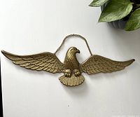 Front view of brass eagle wall hanging showing outstretched wings and hanging chain on a white background.