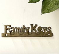 Front view of the vintage brass key rack spelling 'Family Keys' with five hooks underneath the letters.