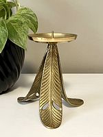 Front view of vintage brass candle holder showing leaf-patterned tripodal base and round holder top with central spike.
