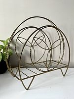 Side angle view of vintage brass magazine rack showing twisted brass circular sides and wire base.
