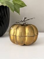 Side view of vintage brass pumpkin trinket holder with decorative stem and leaves on top, showing warm golden patina and slight wear.