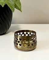 Vintage brass tea light holder shown from an angled front view highlighting multiple heart-shaped cutouts and patina on the surface.