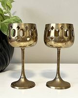 Pair of brass tea light holders side by side, showing full height and cutout pattern on cylindrical cup portion with stem and round base.