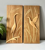 Front view of both wooden wall plaques showing bird and grass relief designs