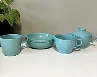 Full view of the vintage Melmac set including all five pieces: two cups, two bowls, sugar bowl with lid, all light blue-green color.