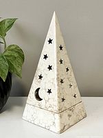 Front view of pyramid-shaped candle holder with star and moon cutouts, showing marbled ceramic texture and celestial design.