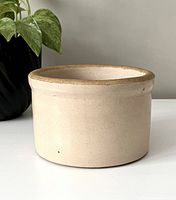 Side view of a small vintage beige crock with unglazed rim, used as decor or planter.