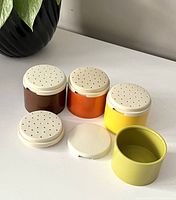 Four vintage Tupperware spice containers shown separated with lids visible, colors brown, orange, yellow, green.