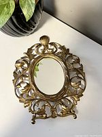 Front view of vintage ornate gold-tone collapsible vanity mirror with decorative leaf and shell motifs around oval mirror.