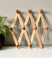 Front view of wooden accordion peg rack expanded with 10 rounded pegs for hanging items.