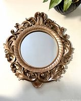 Front view of ornate circular wooden mirror with floral motif and gold finish surrounding round mirror glass.