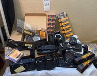 Group view of Nikon F100 bodies, Nikon FM2, Minolta X-700, Miranda AiC, straps and battery pack on table