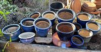 Overview showing 13 blue ceramic pots and two pot movers arranged outdoors