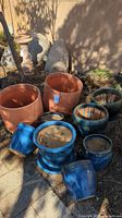 Photo showing the two large terra cotta colored plastic pots and the group of blue glazed ceramic pots in various sizes.